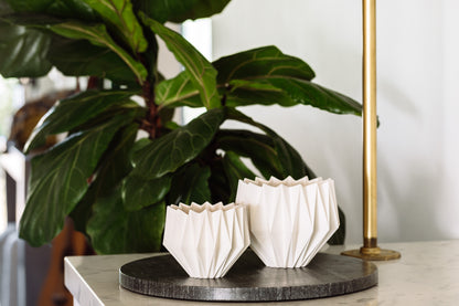 two white vases sit on a marble counter next to a plant